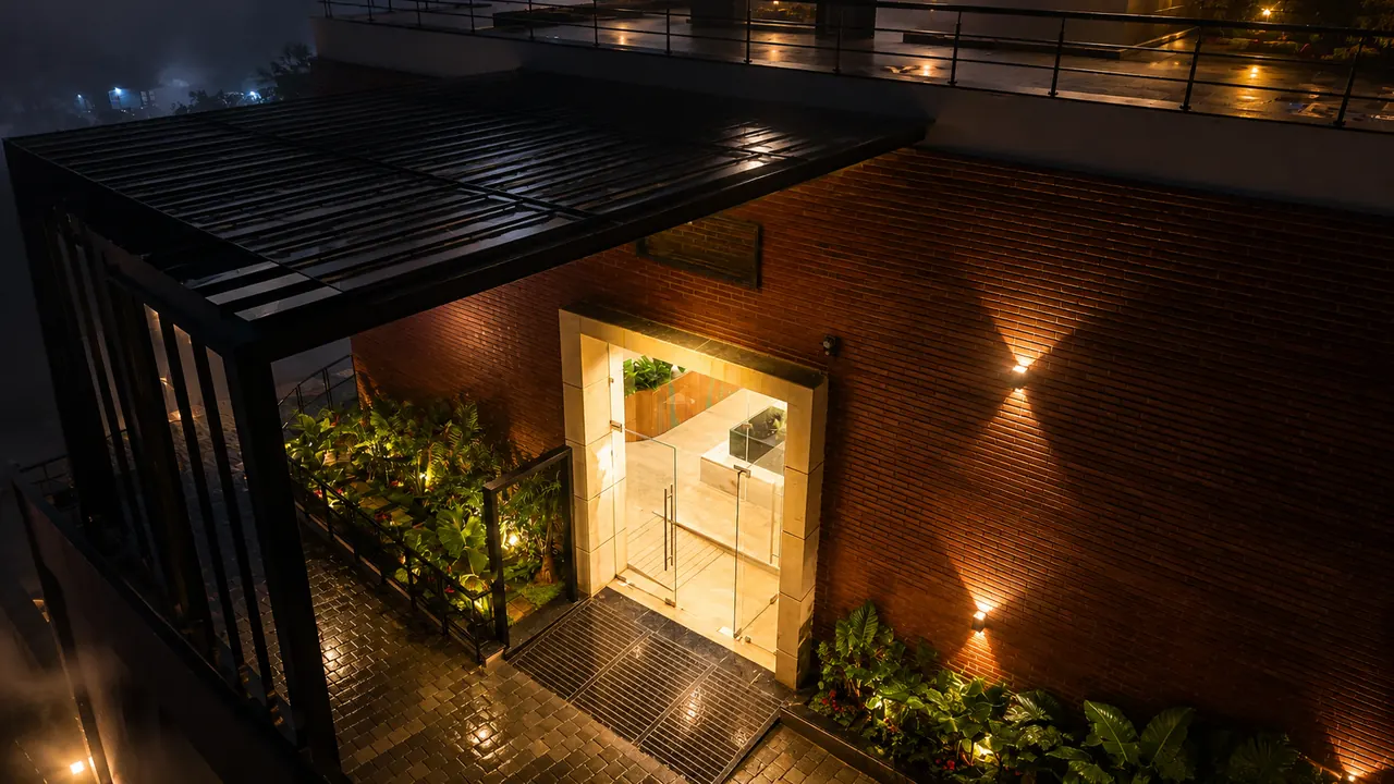 The brick courtyard entrance at night, a warm doorway glowing among the plants