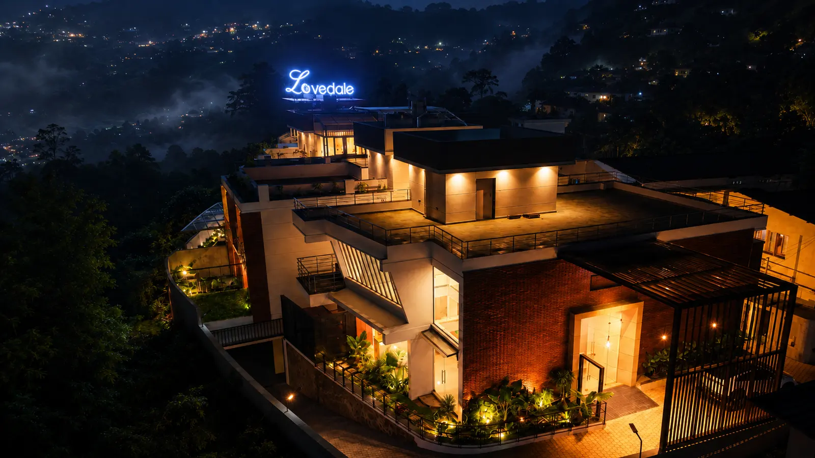 The Lovedale lit up at night, its sign glowing above the lights of Kodaikanal